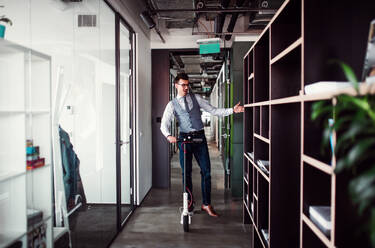 Junger Geschäftsmann mit Motorroller in einem Bürogebäude, der eine Pause macht. - HPIF18405