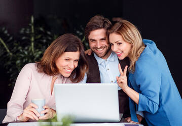 Eine Gruppe fröhlicher Geschäftsleute, die in einem Büro sitzen und einen Laptop benutzen. - HPIF18444