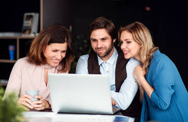 Eine Gruppe fröhlicher Geschäftsleute, die in einem Büro sitzen und einen Laptop benutzen. - HPIF18445