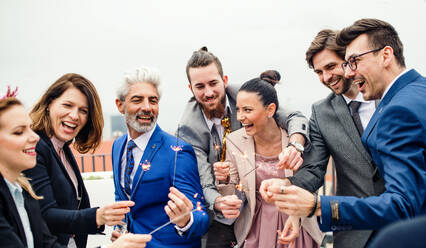 Eine große Gruppe fröhlicher Geschäftsleute feiert auf einer Dachterrasse in der Stadt eine Party mit Wunderkerzen. - HPIF18481