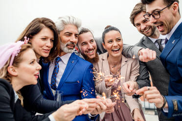 Eine große Gruppe fröhlicher Geschäftsleute mit Wunderkerzen feiert eine Party im Freien auf einer Dachterrasse in der Stadt. - HPIF18482