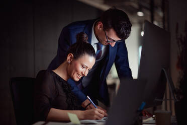 Two young business people in an office in the evening or at night, using computer. - HPIF18494