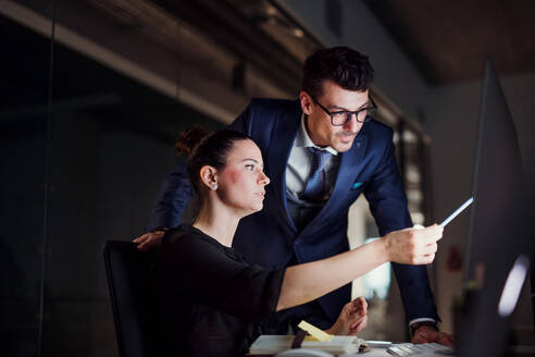 Two young business people in an office in the evening or at night, using computer. - HPIF18497