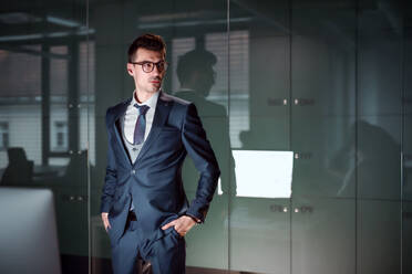Porträt eines jungen Geschäftsmannes, der in einem Büro steht, die Hände in den Taschen, Kopierraum. - HPIF18498