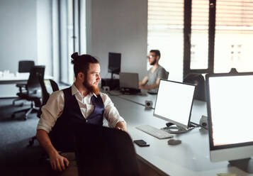 A portrait of young businessman sitting at the table in an office, working. Copy space. - HPIF18500