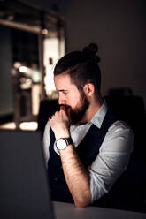 A portrait of young hipster businessman with computer in an office, working. - HPIF18502