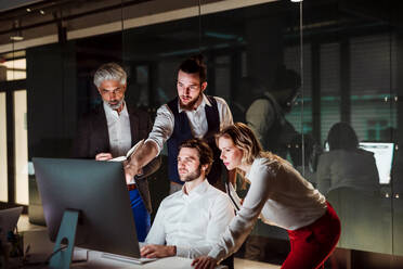 Eine Gruppe von Geschäftsleuten in einem Büro am Abend oder in der Nacht, die einen Computer benutzen. - HPIF18506