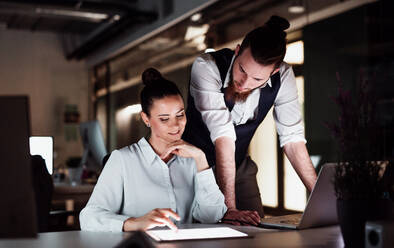 Two young business people in an office in the evening or at night, using computer. - HPIF18508