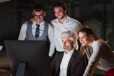 Eine Gruppe von Geschäftsleuten in einem Büro am Abend oder in der Nacht, die einen Computer benutzen. - HPIF18509