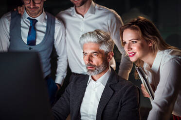 Eine Gruppe von Geschäftsleuten in einem Büro am Abend oder in der Nacht, die einen Computer benutzen. - HPIF18510