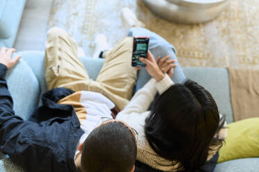 Junges Paar teilt sich ein Smartphone und sitzt zu Hause auf dem Sofa - SOBF00001