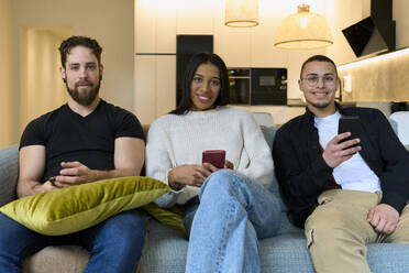 Lächelnde Freunde mit Smartphones auf dem Sofa zu Hause - SOBF00003