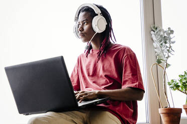 Nachdenklicher Mann mit Headset und Laptop zu Hause - NLAF00005