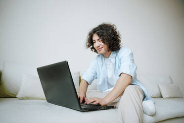 Jugendlicher mit Laptop auf der Couch zu Hause - NLAF00013