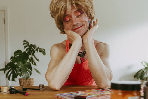 Smiling drag queen leaning on elbows at table in home - OSF01572