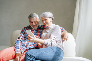 Älteres Paar, das ein Smartphone benutzt und zu Hause auf der Couch sitzt - MDOF01114