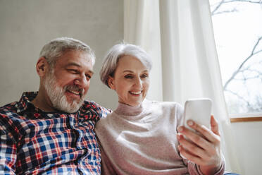 Lächelndes reifes Paar bei einem Videoanruf über ein Smartphone zu Hause - MDOF01116