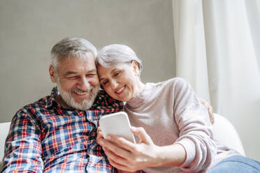 Smiling mature couple using smart phone sitting at home - MDOF01119