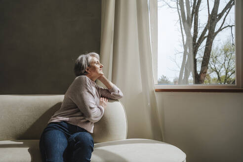 Mature woman relaxing on couch by window at home - MDOF01131