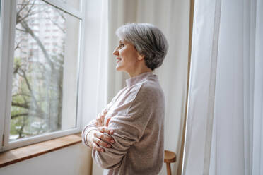 Thoughtful mature woman looking from window at home - MDOF01142