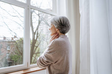 Thoughtful mature woman looking through window at home - MDOF01143