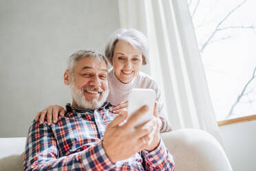 Glückliches reifes Paar im Gespräch über Videoanruf durch Smartphone zu Hause - MDOF01155
