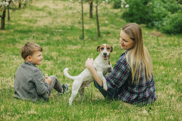 Happy mother and son sitting with Jack Russell Terrier dog in garden - VSNF00905