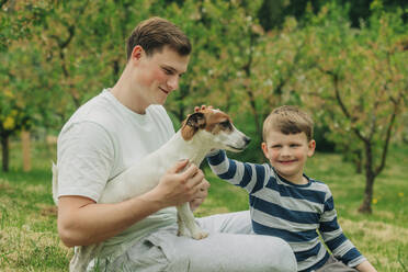 Glücklicher Vater mit Sohn streichelt Jack Russell Terrier Hund im Garten - VSNF00906