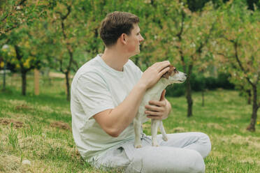 Man sitting with Jack Russell Terrier dog in garden - VSNF00908