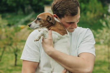 Glücklicher Mann umarmt Jack Russell Terrier Hund im Garten - VSNF00910