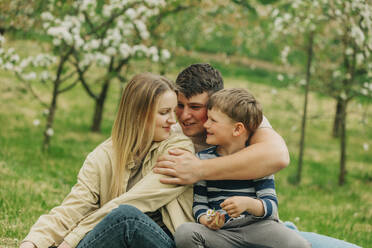 Smiling father and mother with son embracing each other in garden - VSNF00913