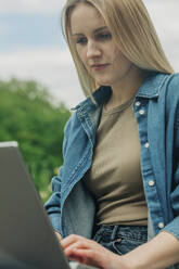 Blonde Frau benutzt Laptop im Garten - VSNF00917