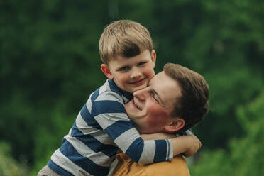 Glücklicher Sohn umarmt Vater im Garten - VSNF00920
