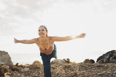 Reife Frau übt Yoga mit ausgestreckten Armen am Strand - AAZF00532