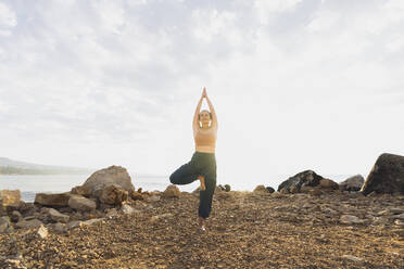 Woman practicing tree pose at beach - AAZF00534