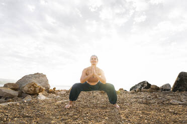 Frau übt Yoga in hockender Position am Strand - AAZF00536