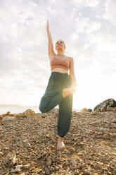 Woman practicing yoga standing on one leg at beach - AAZF00541