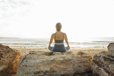 Woman meditating on rock at beach - AAZF00542