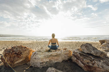 Woman meditating sitting on rock at beach - AAZF00543