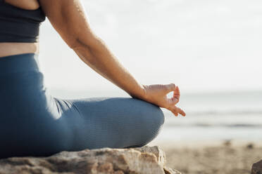 Woman gesturing mudra meditating on rock at beach - AAZF00551