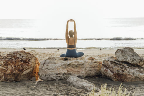 Woman stretching arms on rock at beach in front of sky - AAZF00553