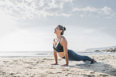 Frau übt Yoga mit Kobra-Pose vor dem Himmel am Strand - AAZF00561