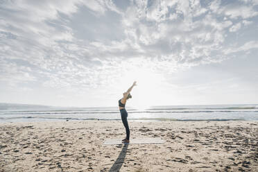 Woman practicing crescent moon pose at beach - AAZF00562