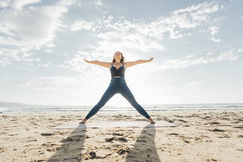 Frau übt Yoga mit ausgestreckten Armen am Strand - AAZF00567