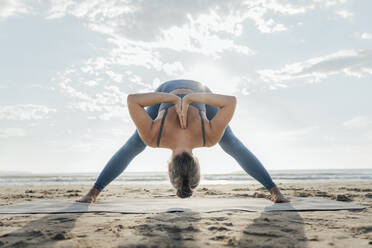 Frau übt Prasarita Padottanasana C Pose Biegen am Strand - AAZF00570