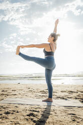 Frau übt Yoga auf einem Bein stehend vor dem Himmel am Strand - AAZF00571