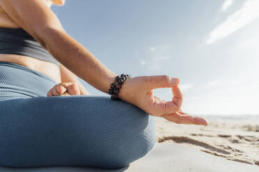 Woman wearing bracelet practicing Lotus position at beach - AAZF00577