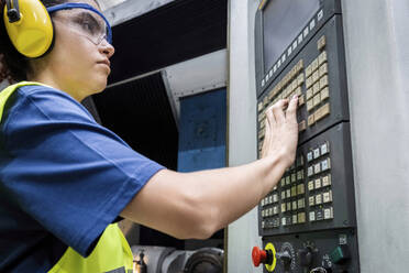 Wartungstechniker in Arbeitsschutzkleidung bei der Bedienung der Tastatur einer CNC-Maschine in einer modernen Fabrik - AAZF00606