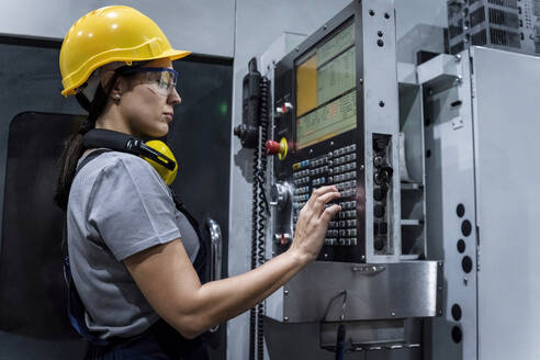 Maintenance engineer wearing hardhat operating machine keypad in modern factory - AAZF00629