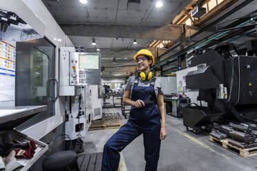 Smiling maintenance engineer standing by CNC machine in modern factory - AAZF00633